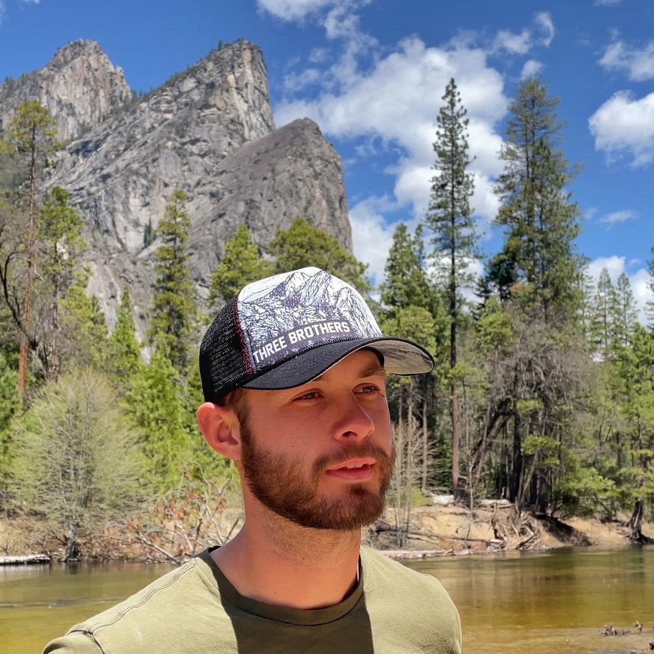 Man wearing a Three Brothers trucker hat in front of Three Brothers mountains | Hiker Sight